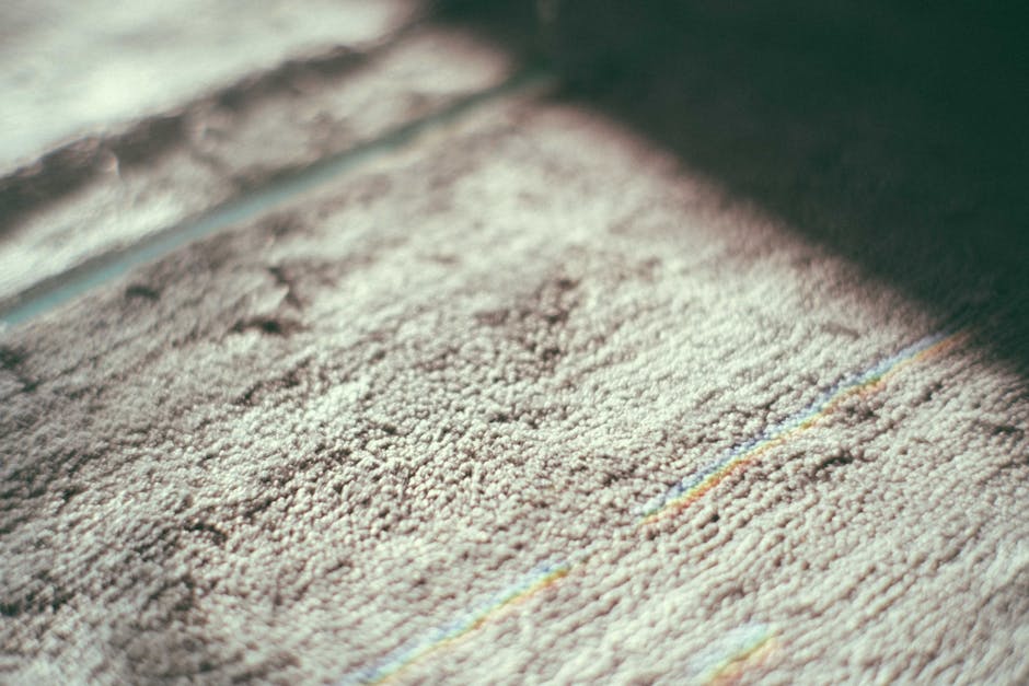 A professional cleaner from Cleaners Finsbury Park wearing a white protective suit, face shield, and blue gloves is performing deep carpet cleaning on a beige rug in a bright, modern living room. The 