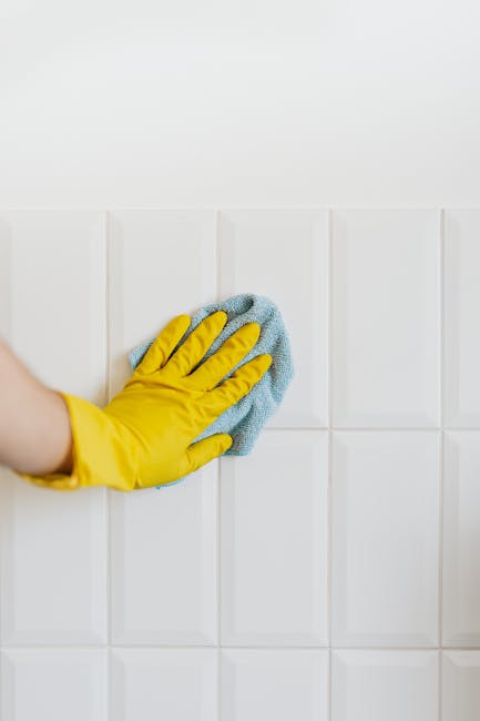 A team of three professional cleaners, dressed in red overalls, are performing surface cleaning and deep cleaning in a modern, bright kitchen with white walls and large glass sliding doors. One cleane